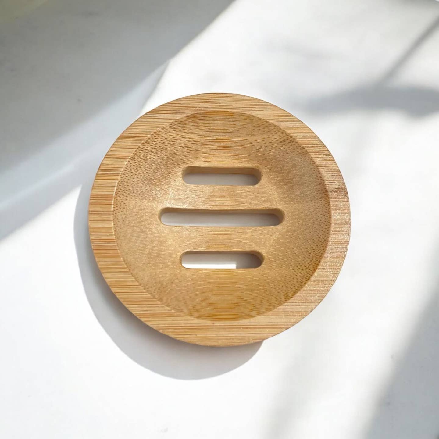 The Soap Dish: Bamboo Shower Steamer Circle Lift, a round bamboo holder with three horizontal drainage slots, rests on a white surface in natural light—ideal as a shower steamer holder.