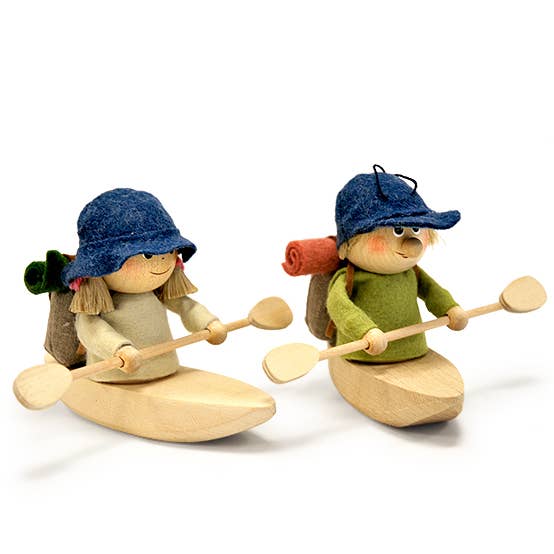 The Scandinavian Hiking Girl in Kayak figurine features two handcrafted figures in blue hats, seated in carved wooden kayaks with paddles and backpacks, ready for an adventure.