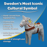 The Dala Horse: "Love Horse" Karlekshast 13cm 5" Approx is a hand-carved, decoratively painted Swedish icon, shown against a blue backdrop to celebrate classic heritage and showcase its unique craftsmanship.