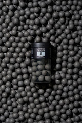 A jar labeled “E” is placed on a surface covered with round, matte black Nordic licorice balls arranged densely as a textured background.