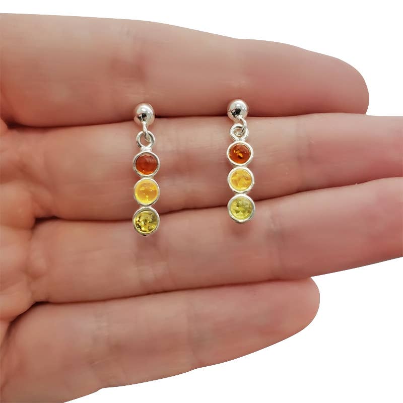 A hand holds the Multi-Color Amber Sterling Silver Post Dangle Earrings, each featuring three round Baltic amber gemstones in yellow, orange, and amber hues.