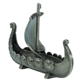 The Faire - Scandinavian Specialties Figurine: Norwegian Viking Ship with Sail Pewter 5″x3″ Table Decor features a silver-toned model of a Viking longship, complete with an intricately detailed dragon head prow, shield decorations lining the sides, and a single mast topped with a sail. Celebrating Scandinavian heritage, this pewter decor piece is showcased on a plain white background.