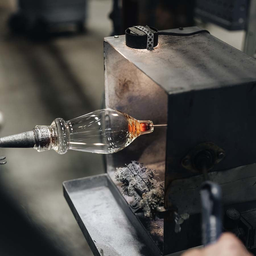 At the Orrefors glassblowing workshop, an artisan expertly shapes molten glass with a blowpipe and metal molds in a furnace, reflecting the artistry of Erika Lagerbielkes Intermezzo Blue Flute 7oz collection.