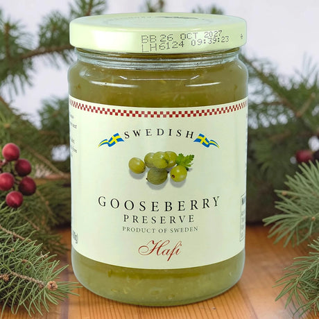 A jar of Swedish gooseberry preserves on a wooden surface, surrounded by pine branches and red berries.