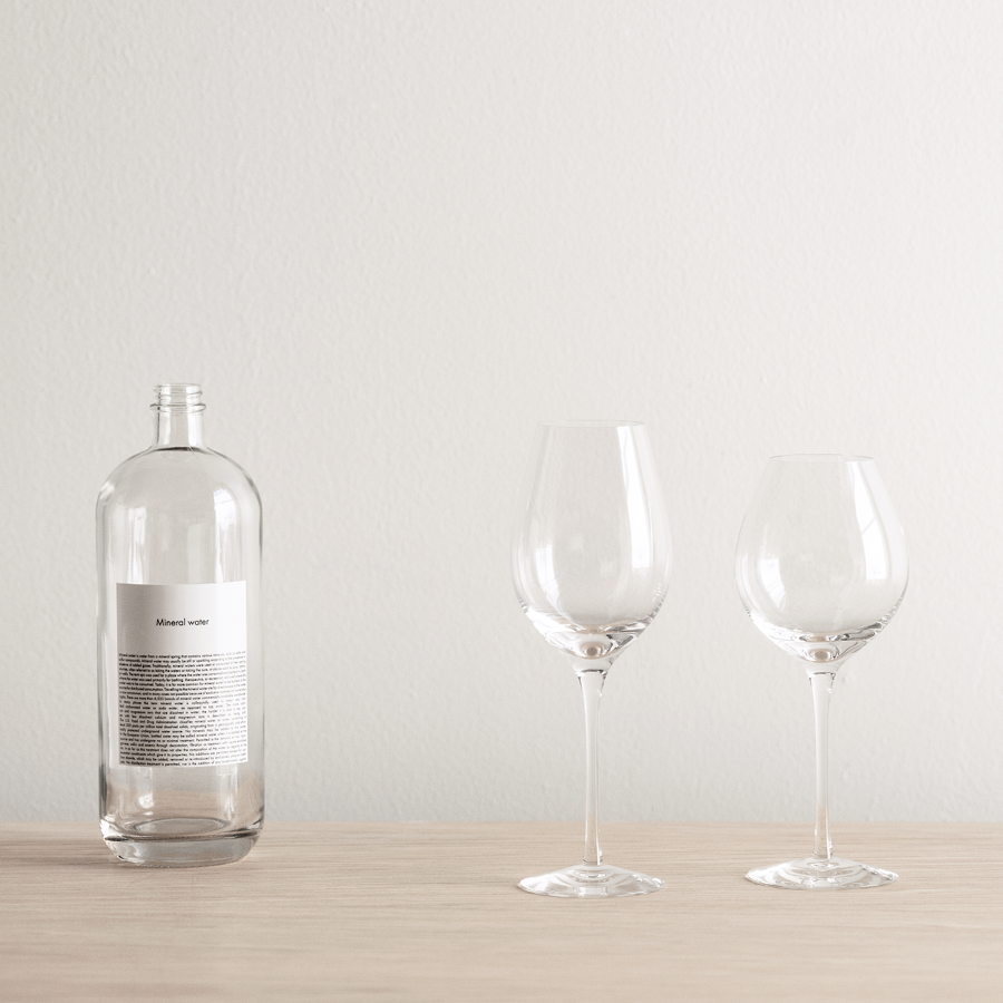 A mouth-blown glass bottle from Sweden with a label sits beside an Orrefors Difference Fruit Glass 2-pack on a wooden surface against a plain white background.