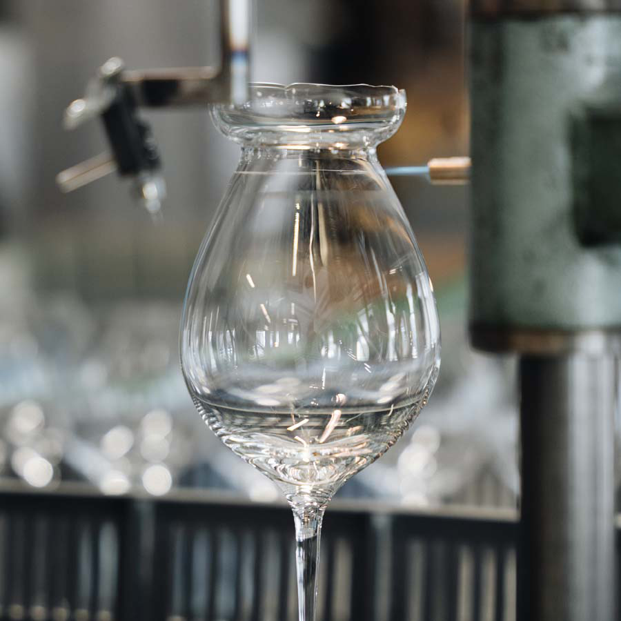 The Orrefors: Difference Fruit Glass (2-Pack) is elegantly shaped in a glassblowing workshop, reminiscent of goblets used for aromatic white wines, and held securely by machinery.