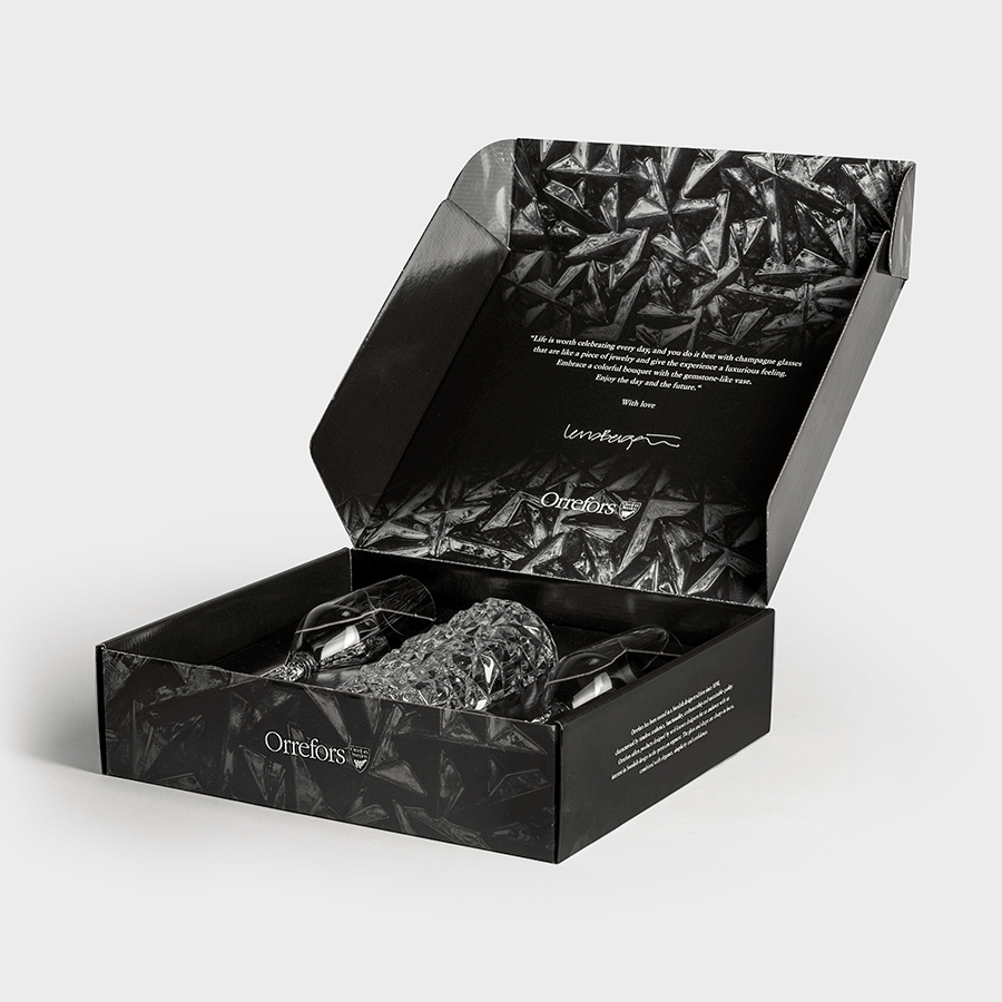 Open the black box to reveal the Orrefors: Carat 3 Piece Gift Set—a stunning pair of textured crystal glass objects nestled on protective material. The lid, adorned with a geometric pattern and elegant text, embodies the sophistication typical of Orrefors design.