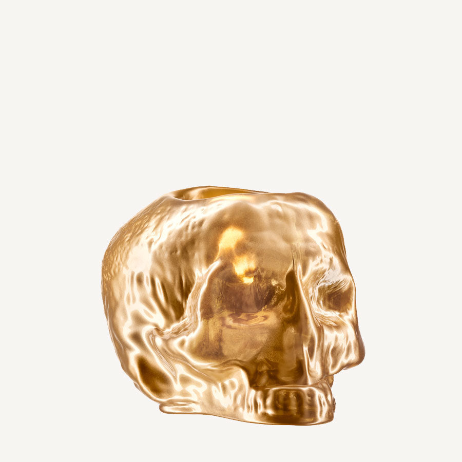 A shiny, metallic gold sculpture of a human skull, like the KostaBoda: Still Life Votive Candle Holder, is set against a plain white background.