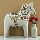 A handcrafted gray Swedish Dala Horse "Anders / Anniversary Series" by Grannas Olsson (13 cm) stands beside a speckled vase with red, gray, and white felt ball stems, all set against a beige background.