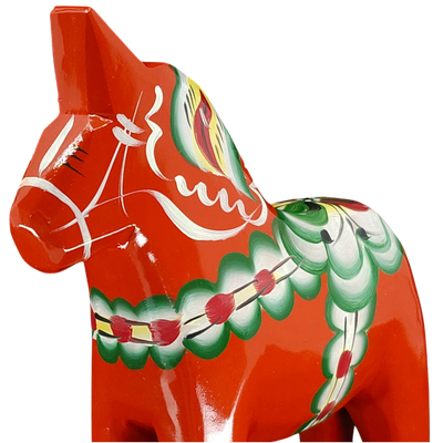 The Red Swedish Dala Horse by Grannas Olsson is handcrafted from Swedish pine and features vibrant green, white, and yellow patterns inspired by traditional Swedish folk art.