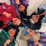 The Walburga Red Kitchen Witch Doll features a colorful, hand-crafted design with wide eyes and a toothy smile, holding a small stick—perfect as a playful good luck charm for your kitchen or home.