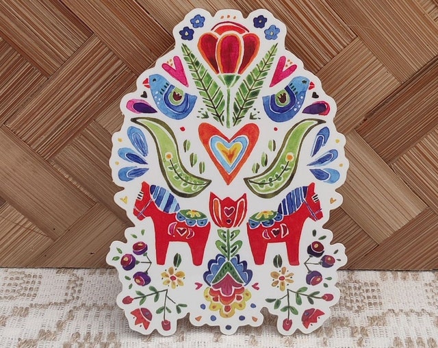 Sticker called "Spring Folk Horses" by Greta Lann showcases lively folk art with colorful birds and detailed folk flowers set against a woven background.