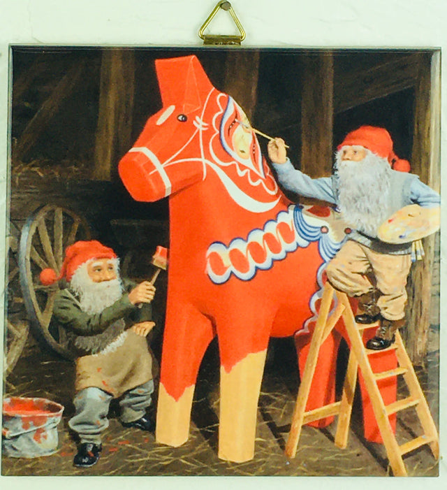 Two white-bearded tomte with red hats, inspired by Jan Berglind, paint a Swedish Dala Horse in a rustic barn on this 6"x6" tile with cork backing & hanger: Tile: Tomte Painting Swedish Dala Horse by Jan Berglind.