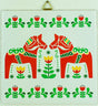 The 6" Tile: 2 Swedish Dala Horses and Swedish Flowers features two red Dala Horses facing each other, surrounded by green leaves and red and yellow floral patterns. It includes cork backing and a hanger for easy display.