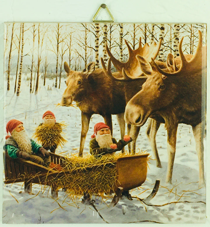 The "Tile: Jan Berglind Moose & Tomten in a Sled" features an enchanting scene of three gnomes wearing red hats on a sleigh with hay, watching two moose in a snowy forest, perfect for adding a whimsical touch to any wall decor.