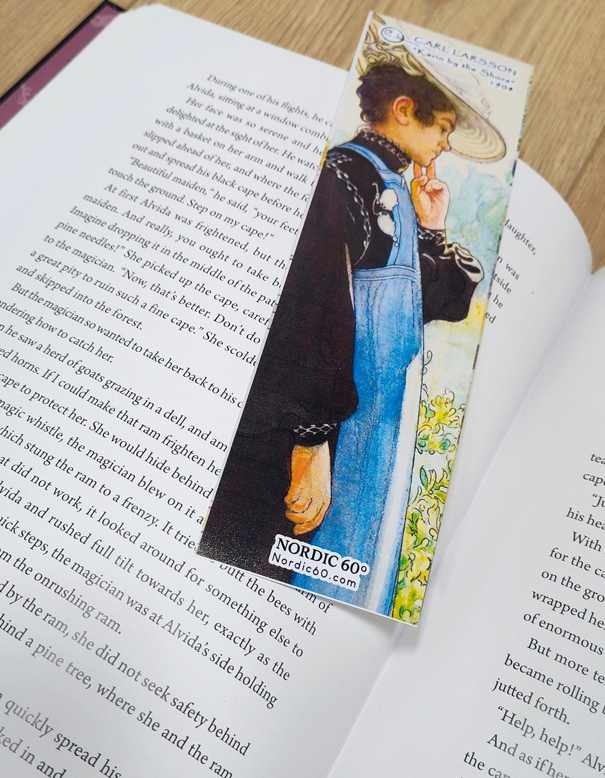 An open book with the Carl Larsson “Karin by the Shore” bookmark (8.5" × 2.5”), capturing Scandinavian countryside charm and artful detail—a nod to Nordic heritage for your reading moments. Labeled NORDIC 600°.