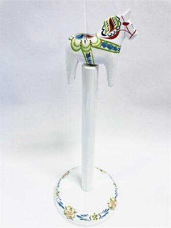 Introducing the Roll Holder: Dala Horse on a Stick, a hand-painted decorative white wooden horse reminiscent of traditional Dala Horses, featuring vibrant red, blue, and green patterns. It stands elegantly on a circular base embellished with floral motifs.