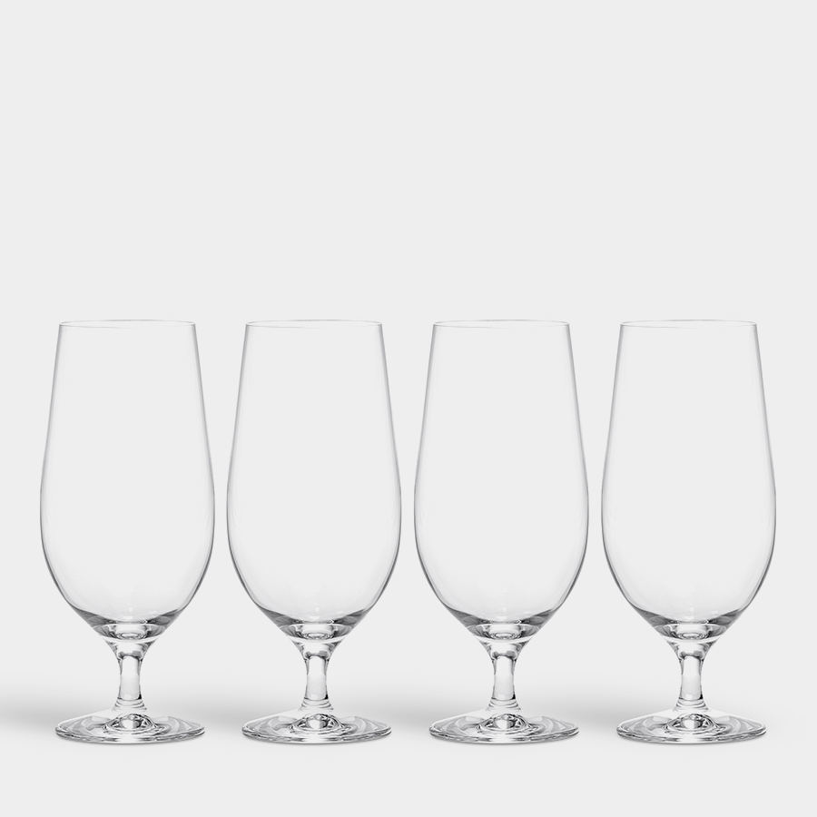 A set of four clear Orrefors Beer Lager 20oz glasses is arranged in a row on a white background, exuding pristine elegance reminiscent of an Erika Lagerbielke design.