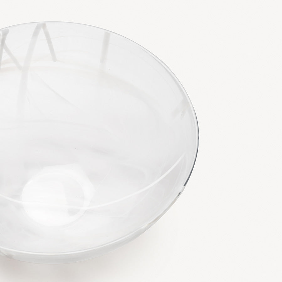 The KostaBoda: Contrast Bowl White glass bowl by Anna Ehrner features a subtle swirl pattern, enhancing elegance in any space. Its transparent design beautifully contrasts with a plain white background.