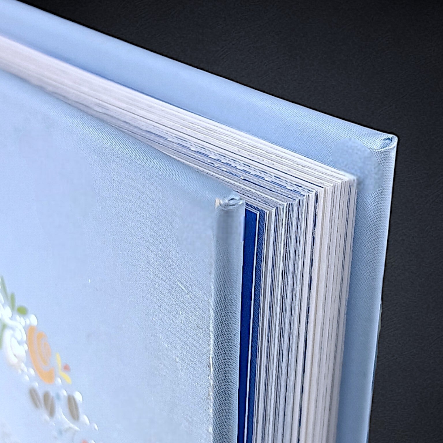 A close-up of the top corner of the closed Little Book of Fika by Lynda Balslev, featuring a textured light blue hardcover and visible white pages—ideal for savoring during a Swedish coffee break or fika with Scandinavian treats.