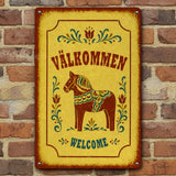 Yellow rectangular welcome sign featuring a red Dala horse, floral rosemaling, and the text VÄLKOMMEN and WELCOME.