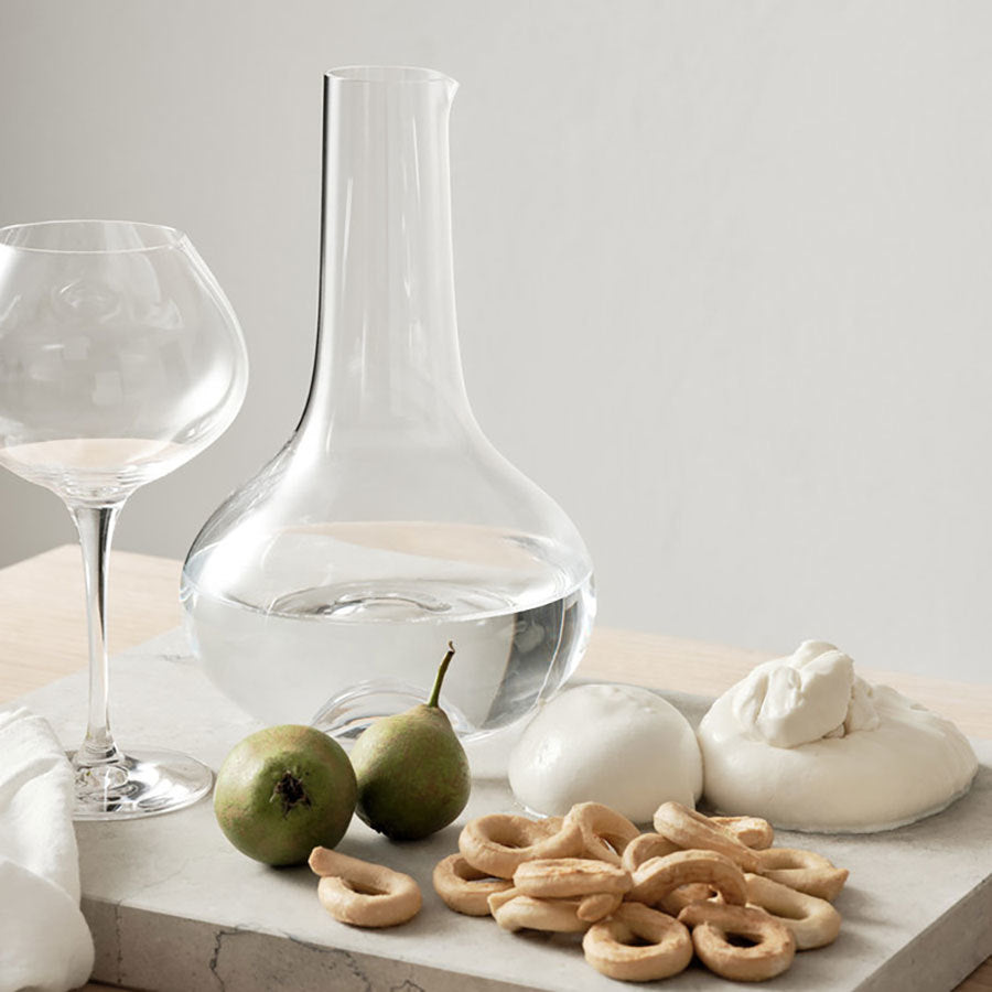 An Orrefors More Mature Glass 16oz from the 4-pack set sits on a table with two green pears, two cheese balls, and a stack of round crackers.