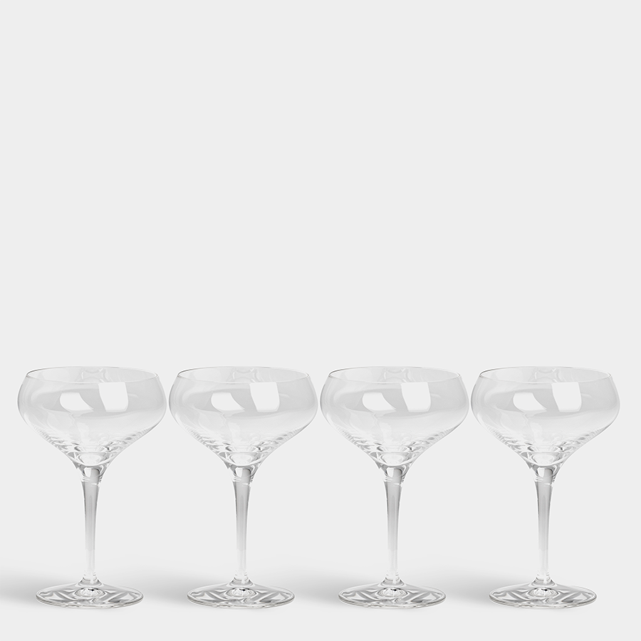 Four clear Orrefors: More Coupe Glasses (7oz, 4-Pack) with wide bowls, designed by Erika Lagerbielke, are lined up against a white background, exuding sophistication and timeless style.