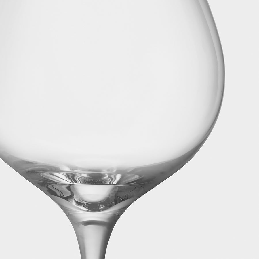 An elegant creation by Erika Lagerbielke for Orrefors, the More Pinot Glass (4-Pack) features smooth curves and a reflective surface, highlighted in a close-up against a plain background.