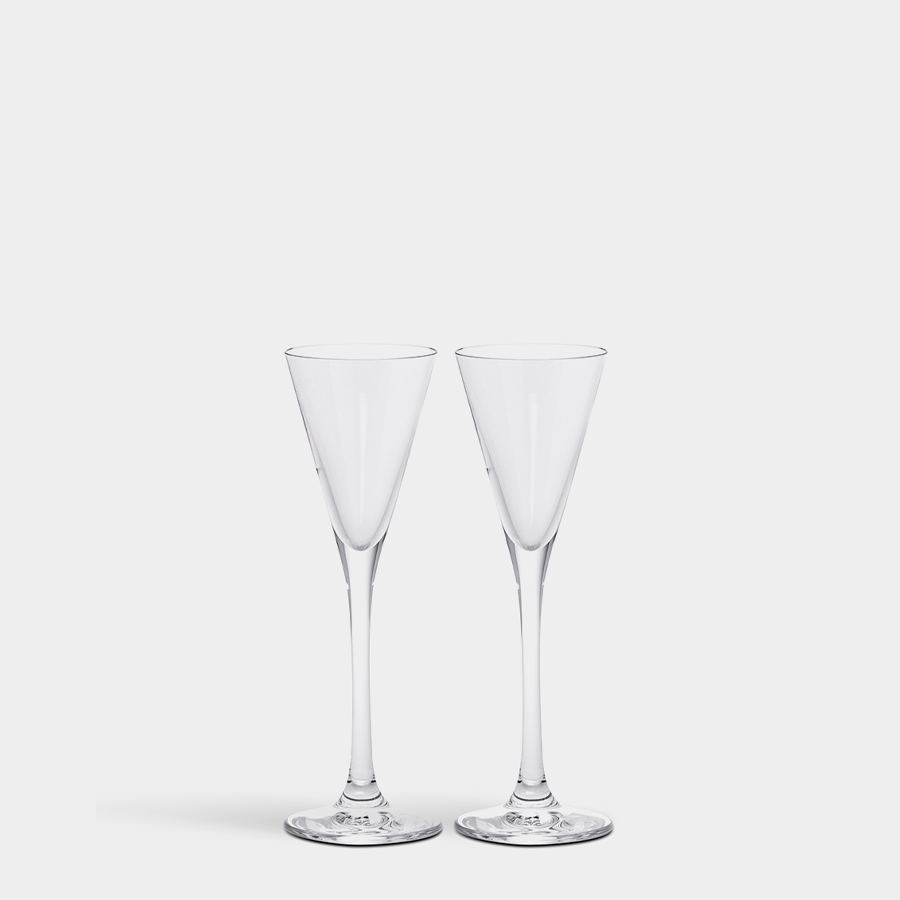 Two empty, clear Orrefors More Snaps glasses (3oz) with long stems and conical bowls are elegantly placed side by side against a plain, light background.