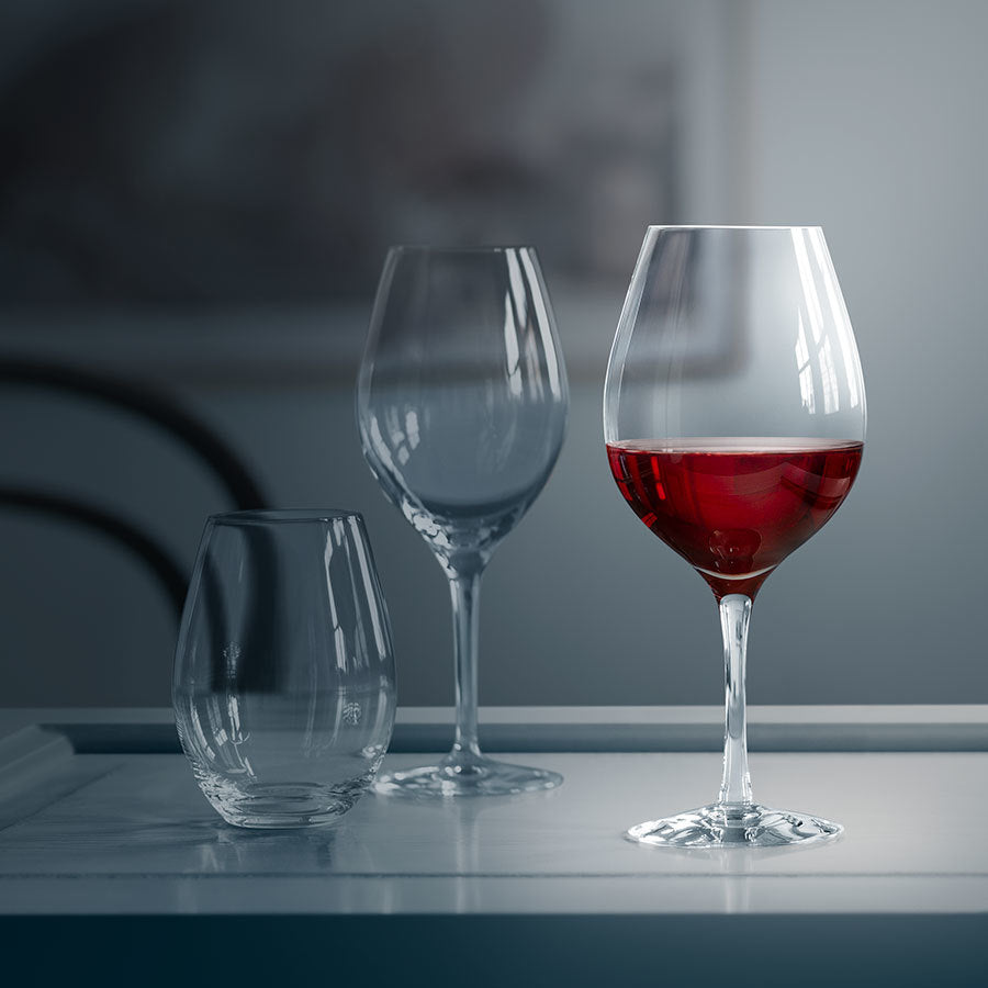 Three wine glasses rest elegantly on the table; one filled with red wine and two empty Orrefors: More Tumbler Glasses from the 13oz 4-Pack awaiting their share.