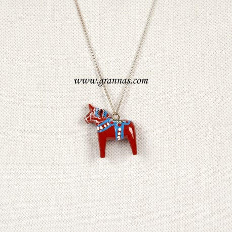 The Necklace: Red Swedish Dala Horse Necklace with Silver Chain showcases a handcrafted pendant of a Red Swedish Dala Horse with blue and white patterns on a light textured background, elegantly hanging from a delicate silver chain.