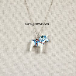 The White Swedish Dala Horse Necklace features a charming pendant with blue and red accents on a sterling silver chain, elegantly displayed against a textured beige background.