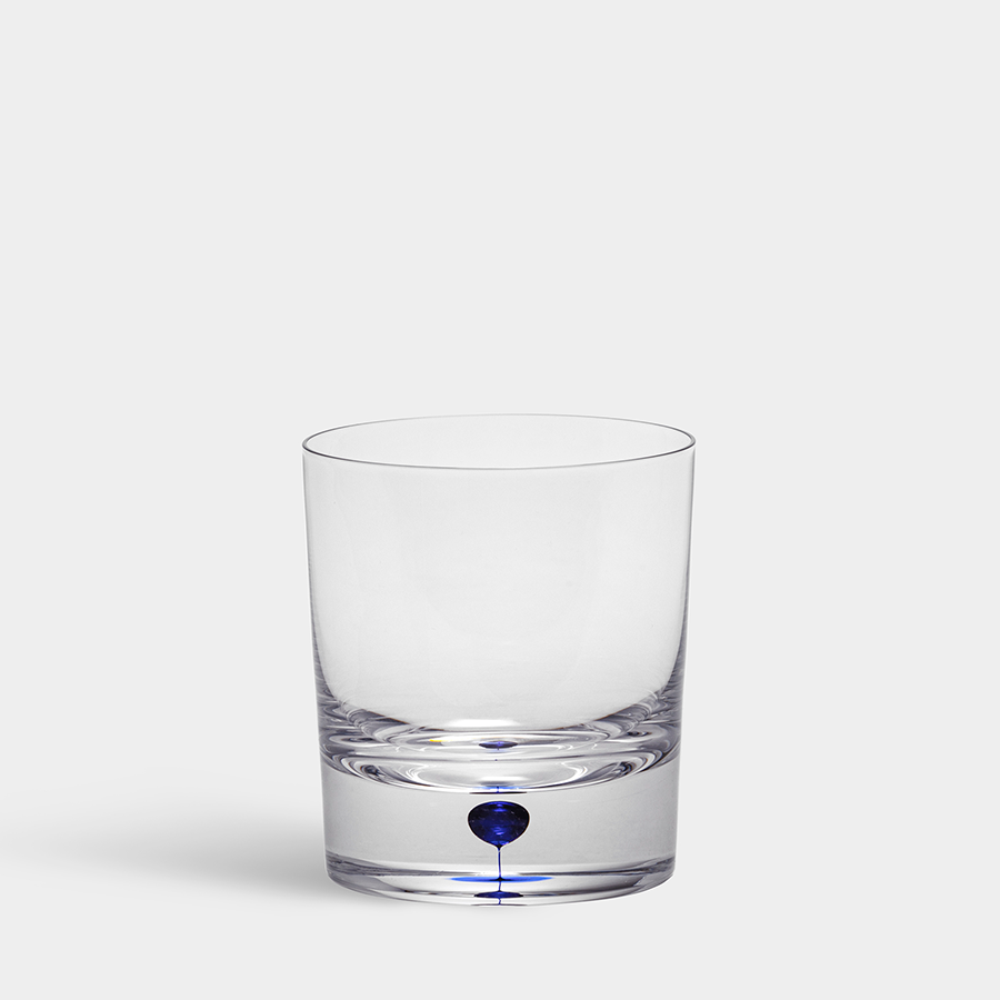 The Orrefors Intermezzo Blue Old Fashioned/Whiskey Glass 8.5oz, designed by Erika Lagerbielke, features clear glass with a thick base and showcases a small blue sphere on a light grey background.