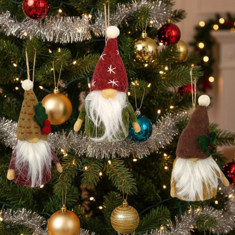 Three felt gnome Christmas ornaments with long white beards hang from a tree decorated with red, gold, and blue baubles and silver garland.