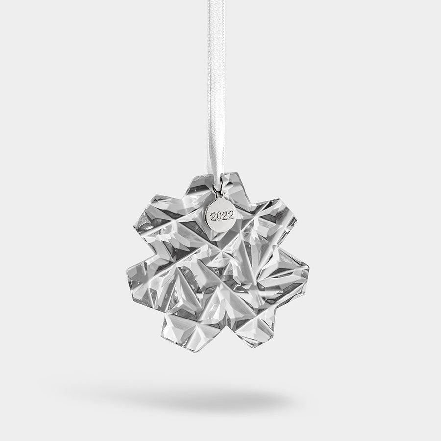 The Orrefors: Annual Ornament Carat 2022 gracefully hangs from a white ribbon against a simple backdrop.