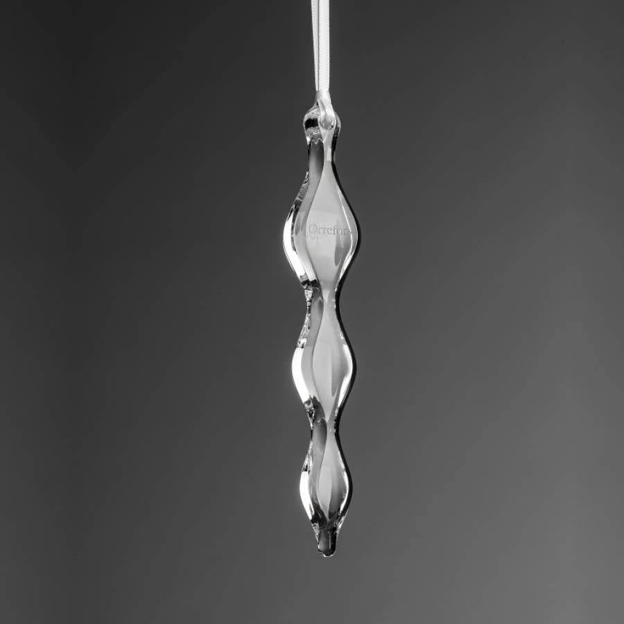 The Orrefors: The Ornament Icicle, a clear glass ornament, hangs vertically against a gray background with a white ribbon gracefully attached at the top.