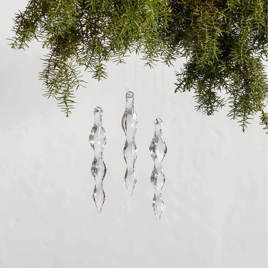 Three Orrefors: The Ornament Icicle twisted glass ornaments hang elegantly from the green branches of a fir tree against a plain white background.