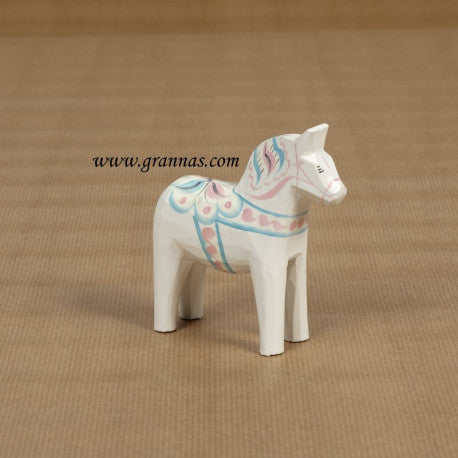 The 10cm hand-painted white Dala Horse, decorated with pastel Kurbits patterns, rests on a textured brown surface, making it an ideal gift.