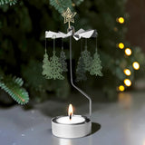 Rotary candle holder with a lit tealight and hanging Christmas tree-shaped ornaments, displayed in front of a blurred, illuminated Christmas tree.