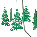Green metal ornaments with cut-out designs hang from thin rods on a chrome Swedish rotary candle holder, with part of the stand visible on the right side.
