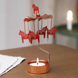 Rose gold Dala horse rotary candle holder with a lit tealight on a wooden table, Scandinavian decor visible in the softly lit background.