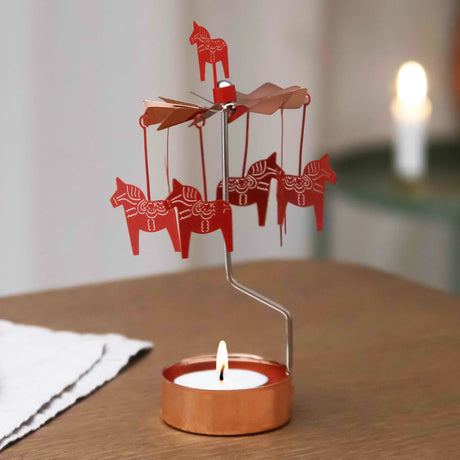 Rose gold Dala horse rotary candle holder with a lit tealight on a wooden table, Scandinavian decor visible in the softly lit background.