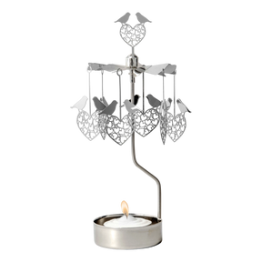 Rotary candle holder with love bird and heart shapes suspended above a lit tealight, all crafted from silver-toned recycled metal.