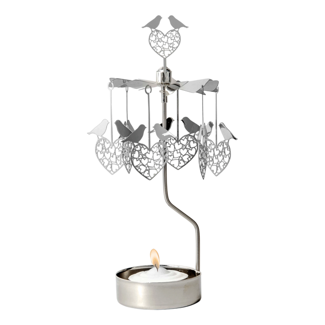 Rotary candle holder with love bird and heart shapes suspended above a lit tealight, all crafted from silver-toned recycled metal.