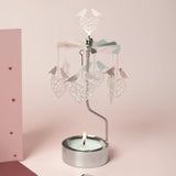 Silver rotary candle holder with hanging love bird and heart ornaments, positioned above a lit tealight candle on a pink background.
