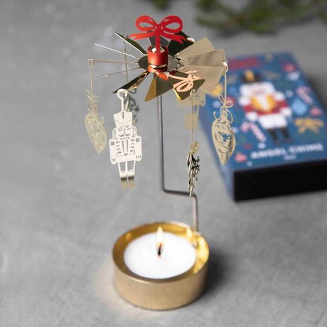 Gold-colored nutcracker candle carousel with hanging ornaments and a lit tea light.