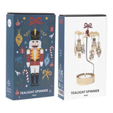 A metal Swedish rotary candle holder with hanging nutcracker ornaments, shown next to its blue illustrated packaging box.