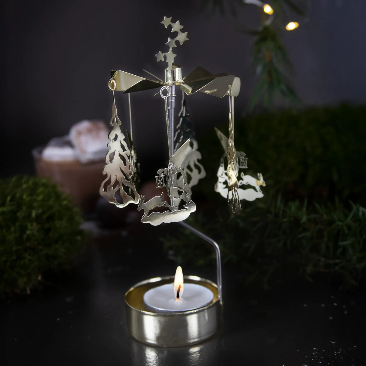 Gold-toned metal rotary candle holder with hanging tree and rabbit ornaments and a lit tealight at the base.