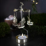 Gold-toned metal rotary candle holder with hanging tree and rabbit ornaments and a lit tealight at the base.