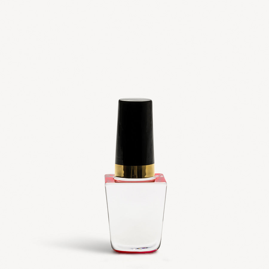 The KostaBoda: Nail Polish Poppy Red bottle, echoing Åsa Jungneliuss artistry, resembles Kosta Boda craftsmanship with its clear glass design and sleek black cap adorned with a gold band. It sits elegantly against a plain white backdrop.